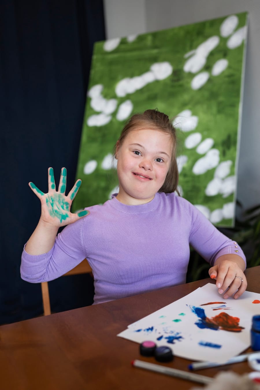 A young girl with Down syndrome smiling while finger-painting at a table