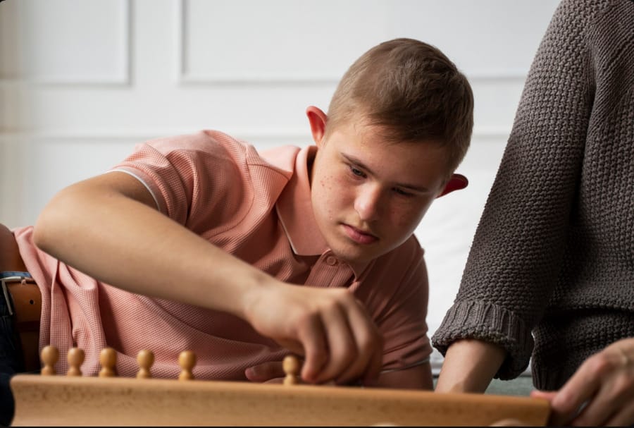 Young man focused on a wooden peg board activity with a caregiver nearby