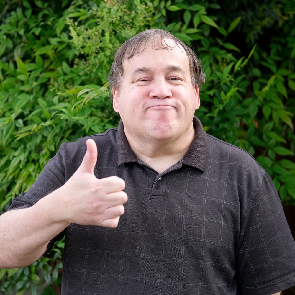 Man giving a thumbs up and smiling in his garden at home
